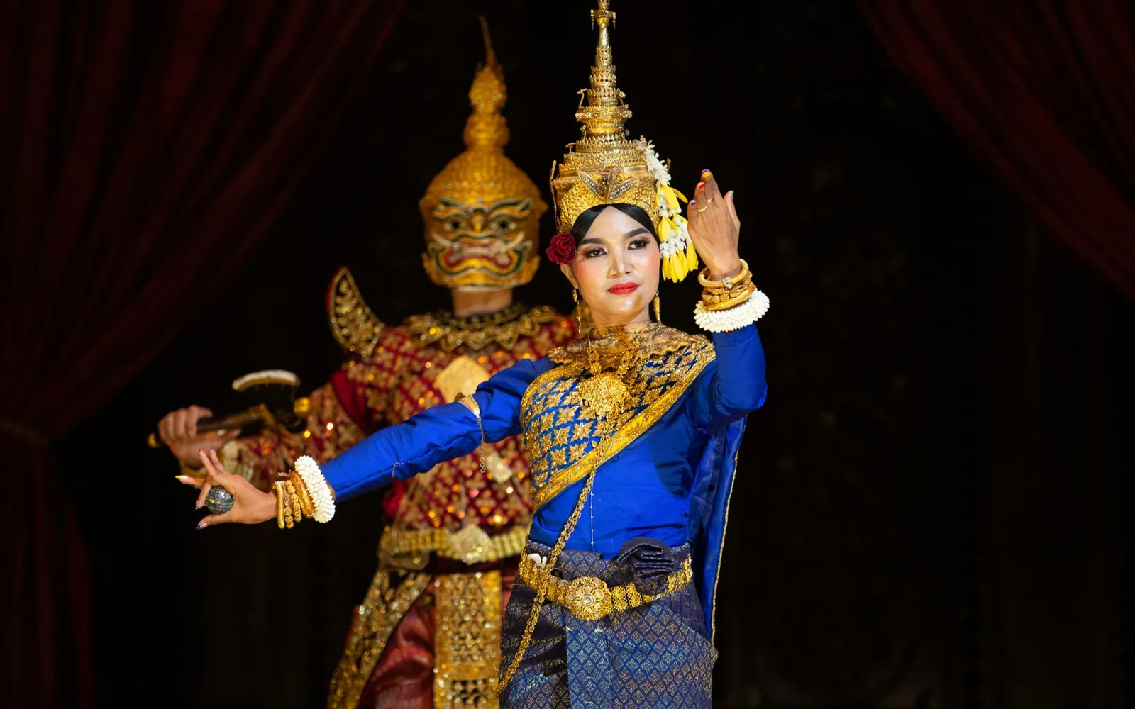 Apsara dancers in classical costume perform on a candlelit stage